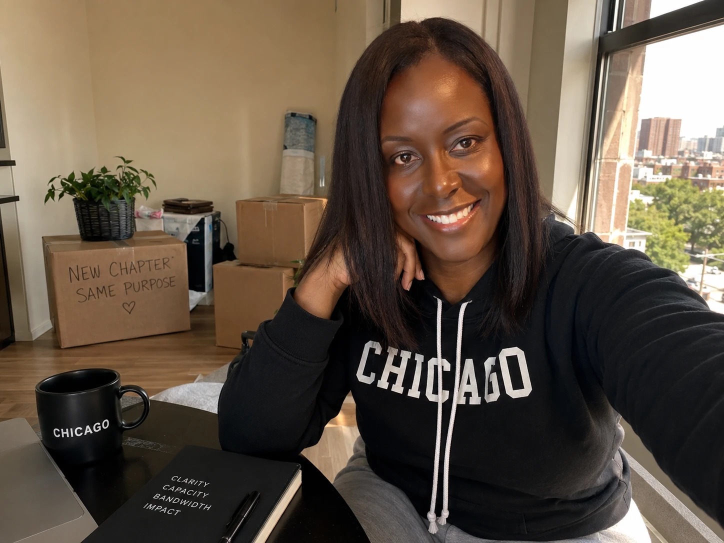 Samone Davis, smiling at her desk among moving boxes — one marked 'New chapter, same purpose'